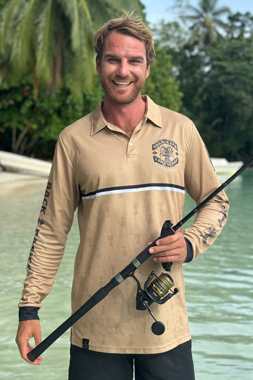 Man holding a fishing rod by a body of water with greenery in the background