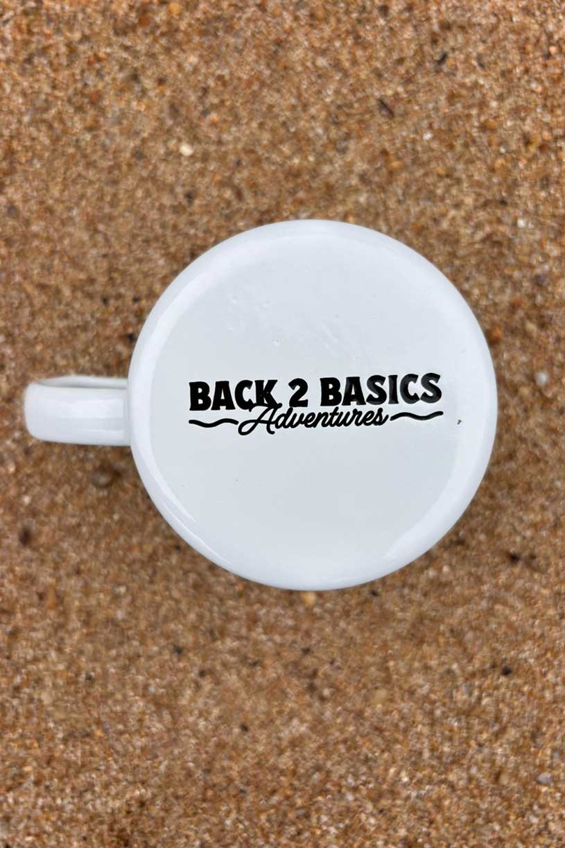 White mug with 'Back 2 Basics Adventures' text on a sandy background
