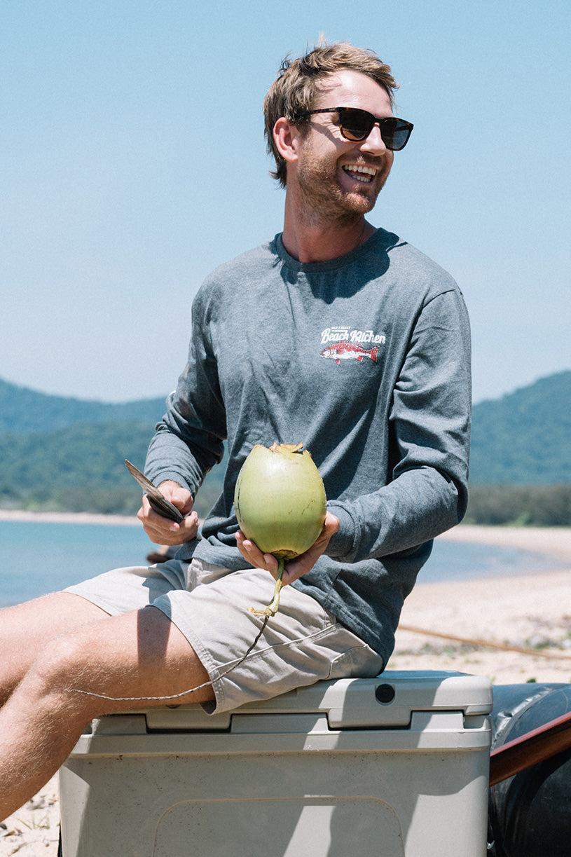 Man holding a green fruit by a body of water with mountains in the background
