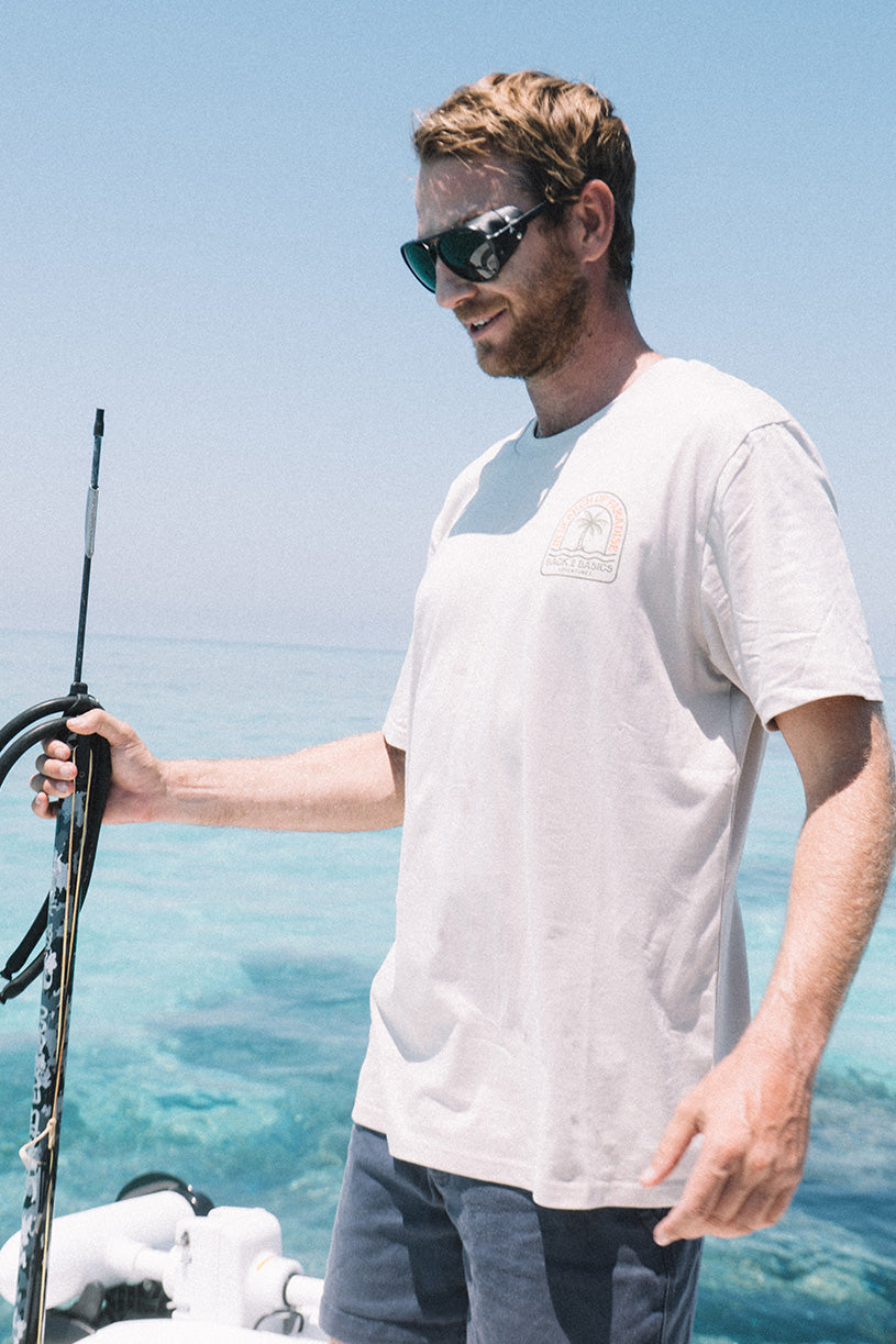 Man on a boat holding a speargun with clear blue sky and water in the background